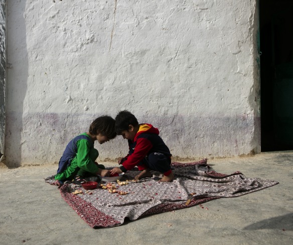 Two boys sit with their heads together on a blanket.