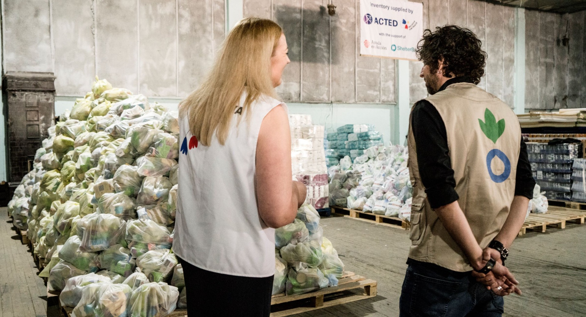 Two aid workers in a warehouse full of emergency supplies to help Ukrainian refugees.